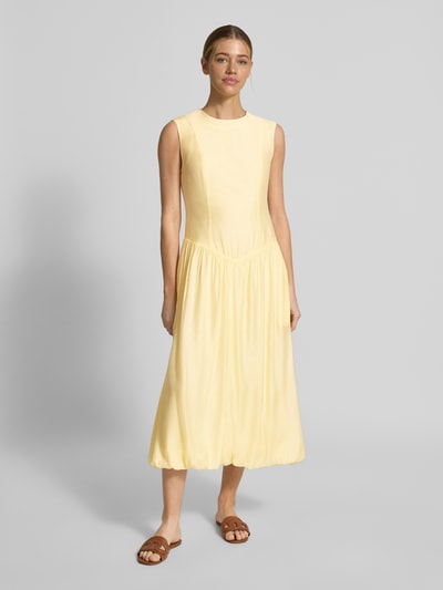 Kobiece modelka nosi żółtą sukienkę Bubble Kleid mit Rundhalsausschnitt Modell 'KRISSI' od YAS, materiał z lyocellem, krój taliowany, długość midi, z okrągłym dekoltem i zamkiem z tyłu, długość pleców w rozmiarze 36: 45 cm, szerokość w rozmiarze 36: 43 cm, gładka tekstura, widok całej sylwetki z przodu.
