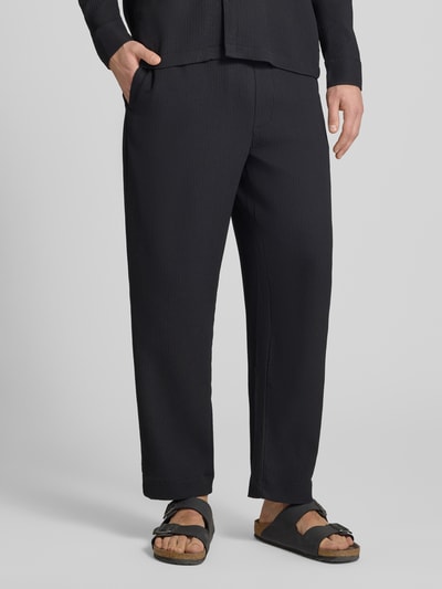 Männermodel trägt Hose mit elastischem Bund in Plissee-Optik von REVIEW, Schwarz, Regular-Fit, Material-Mix mit Stretch-Anteil, Nahaufnahme Unterkörper.