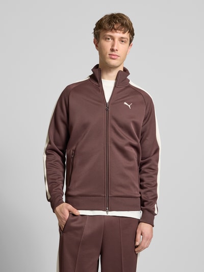 Männermodel trägt Sweatjacke mit Label-Print von PUMA PERFORMANCE in Braun mit weißen Streifen, Regular Fit, Stehkragen, Vorderansicht Oberkörper. Material-Mix mit Baumwoll-Anteil, gerippte Abschlüsse, Reißverschlusstaschen, Rückenlänge 73 cm, Ärmellänge 52 cm.