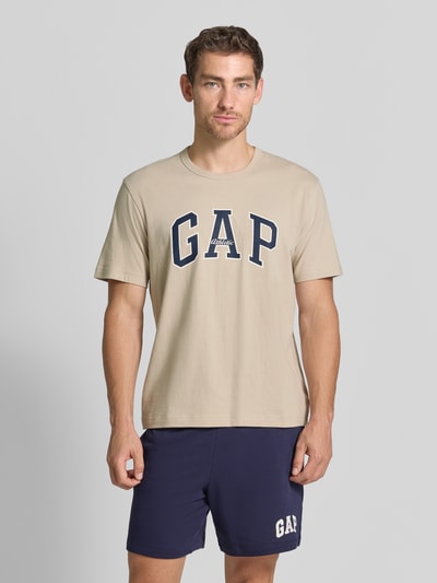 Mannelijk model draagt T-shirt met logo-print en ronde hals van GAP in beige, puur katoen, regular fit, ruglengte maat M 67 cm, geheel aanzicht van voren.