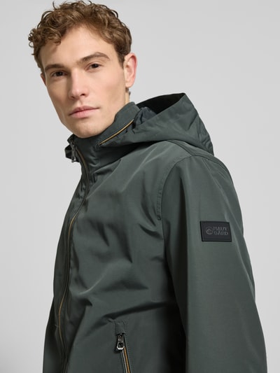 Männermodel trägt Regular Fit Jacke mit Kapuze Modell 'Como' von NAUTGÅRD in Dunkelgrün, sichtbarer Zweiwegereißverschluss, Nahaufnahme Oberkörper.