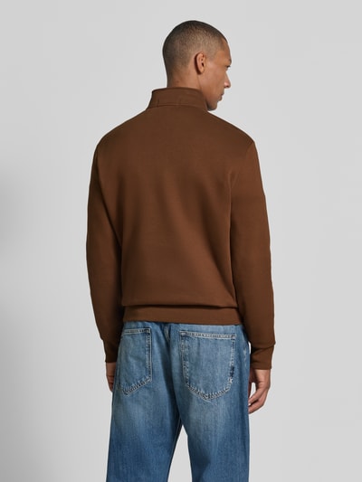 Mannelijk model draagt Relaxed Fit schipperstrui uit katoenmix van Polo Ralph Lauren in bruin met blauwe jeans, geheel van achteren. Heren