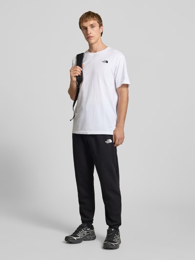Männermodel trägt Sweatpants mit Logo-Print von The North Face in Schwarz, Baumwoll-Mix, Slim-Fit, Elastischer Bund mit Kordelzug, Ganzkörperansicht von vorne.