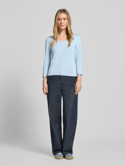 Kobieta nosi Longsleeve mit 3/4-Arm Modell 'Kirosa Fine' od Someday z mieszanki wiskozy i elastanu, krój regular fit, jasnoniebieski na tle szarym, okrągły dekolt, długość tyłu 54 cm w rozmiarze 36, pełen widok z przodu.