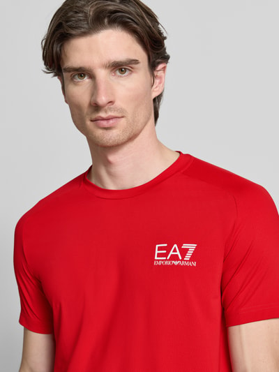 Männermodel trägt T-Shirt mit Label-Print von EA7 Emporio Armani in Rot, gerippter Rundhalsausschnitt, Nahaufnahme Oberkörper.