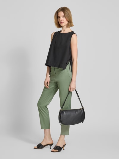 Frauenmodel trägt Slim Fit Stoffhose in verkürzter Passform von Christian Berg Woman aus elastischem Baumwoll-Mix in Grün mit Eingrifftaschen und Gesäßtaschen, kombiniert mit schwarzem Top und Tasche, Ganzkörperansicht von vorne.