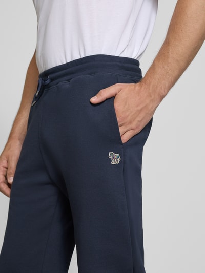 Männermodel trägt Slim Fit Sweatpants aus reiner Baumwolle von Paul Smith in Dunkelblau mit Logo-Stickerei, Nahaufnahme Oberkörper. Elastikbund mit Tunnelzug, seitliche Eingrifftaschen und Gesäßtaschen, Innenbeinlänge bei Größe M 43 cm.