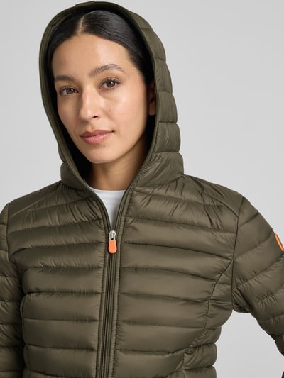 Frauenmodel trägt olivgrüne Steppjacke mit Kapuze Modell 'DAISY' von Save The Duck, Zweiwege-Reißverschluss, Nahaufnahme Oberkörper.