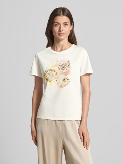Frauenmodel trägt T-Shirt mit Motiv-Print und Strasssteinbesatz von Marc Cain aus Reine Baumwolle, Regular-Fit, Rundhalsausschnitt, Rückenlänge 57 cm, beige Farben, glatte Struktur, Ganzkörperansicht von vorne.
