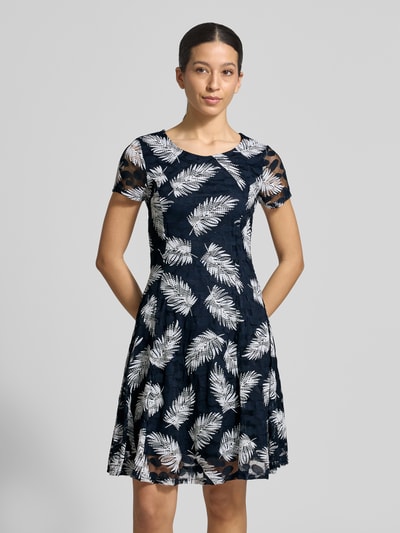 Vrouwenmodel draagt Knielanges Kleid mit Rundhalsausschnitt van Apricot in donkerblauw met witte bladprint, getailleerde fit, stretchmateriaal, knielengte, korte mouwen, ruches, vooraanzicht halflichaam.