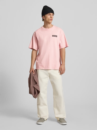Männermodel trägt T-Shirt mit Logo und Rundhalsausschnitt von Dickies in Rosa aus Reine Baumwolle, Relaxed-Fit, Modell 'BUCHTELL', Ganzkörperansicht von vorne.