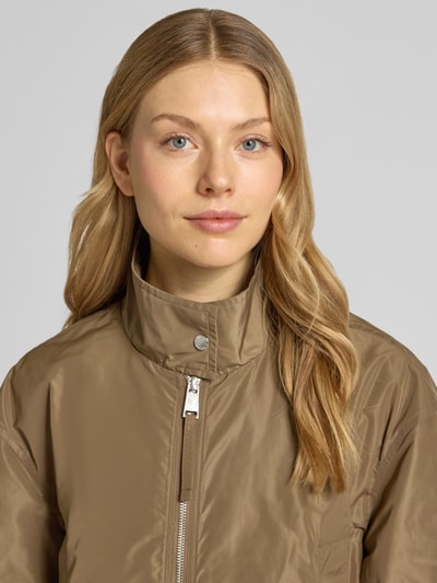 Vrouwenmodel draagt Jacke mit Zweiwege-Reißverschluss und Stehkragen van Fuchs Schmitt in lichtbruin, recht model, elastische mouwuiteinden, staande kraag, metalen rits, gladde structuur, maat 36 met ruglengte 61 cm, schouderbreedte 49 cm, borstwijdte 56 cm, mouwlengte 56 cm, close-up bovenlichaam vooraanzicht.