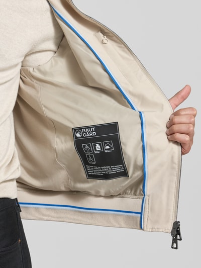 Männermodel trägt Regular Fit Jacke mit Kapuze von NAUTGÅRD in Beige, glatte Struktur, Twowegereißverschluss, Detailaufnahme Innenansicht.