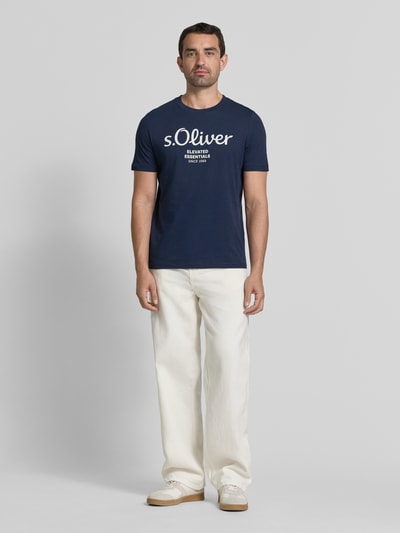 Męski model nosi Regular Fit T-Shirt aus reiner Baumwolle Modell 'BASIC TEE BIG LOGO' von s.Oliver RED LABEL, granatowy z białym nadrukiem, gładka tekstura, proste formy, Ganzkörperansicht von vorne.