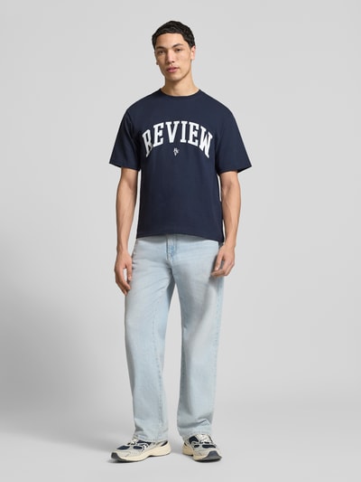Männermodel trägt T-Shirt mit Label-Print und Rundhalsausschnitt von REVIEW in Dunkelblau, Reine Baumwolle, Regular-Fit, Ganzkörperansicht von vorne. Rückenlänge bei Größe M: 65 cm.