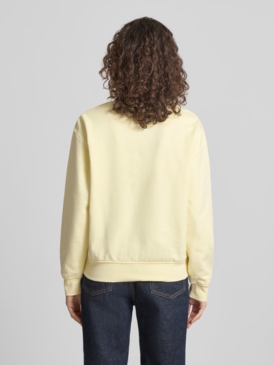 Frauenmodel trägt Sweatshirt mit Label-Print Modell 'GRAPHIC' von Calvin Klein Jeans in Pastellgelb, lockere Passform, Ganzkörperansicht Rückansicht.