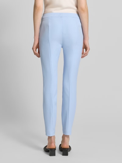 Frauenmodel trägt Slim Fit Hose mit Bügelfalten Modell 'HAGONIA-1' von HUGO in hellblau, unifarben, mit seitlichen Eingrifftaschen, Ganzkörperansicht Rückansicht.