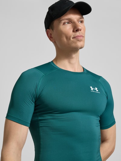 Männermodel trägt Slim Fit T-Shirt mit Logo-Print von Under Armour in Grün, elastischer Material-Mix, Rundhalsausschnitt, Nahaufnahme Oberkörper.