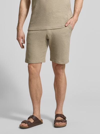 Mężczyzna nosi Regular Fit Poloshirt aus Baumwoll-Mix von MCNEAL, mieszanka bawełny i elastanu, pika, krój regular fit, wykładany kołnierz z dekoltem w serek, krótkie rękawy, długość tyłu 69 cm dla rozmiaru M, kolor beżowy, tekstura waflowa, widok całej sylwetki z przodu.