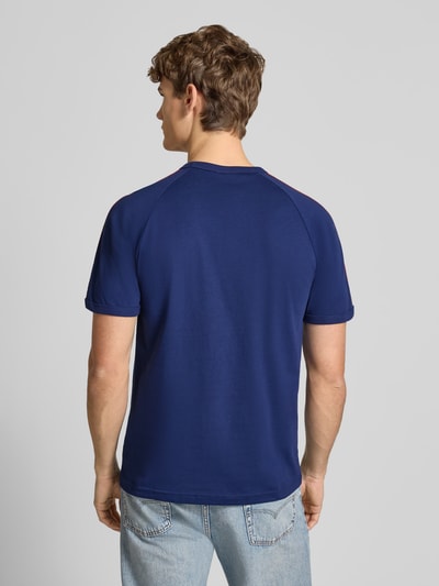 Mężczyzna nosi T-Shirt mit Label-Stitching von adidas Originals w kolorze niebieskim, czysta bawełna, krój regular fit, ściągacze, okrągły dekolt, długość tyłu w rozmiarze M: 74 cm, widok całej sylwetki z tyłu.