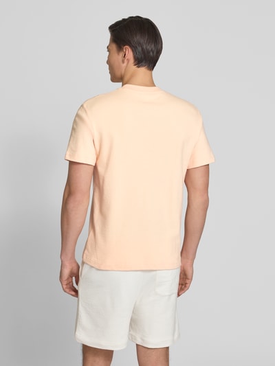 Männermodel trägt Regular Fit T-Shirt aus reiner Baumwolle von Lacoste in hellem Apricot, unifarben, Feinstrick, Ganzkörperansicht Rückansicht.