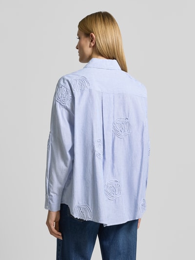 Frauenmodel trägt Relaxed Fit Bluse mit Streifenmuster Modell 'Dalma Dori' von Neo Noir aus reiner Baumwolle mit floralen Applikationen, Hemdblusenkragen, Rückenlänge 73 cm, Ärmellänge 60 cm, dezente blaue und weiße Farbkombination, strukturierte Oberfläche, Ganzkörperansicht Rückansicht.
