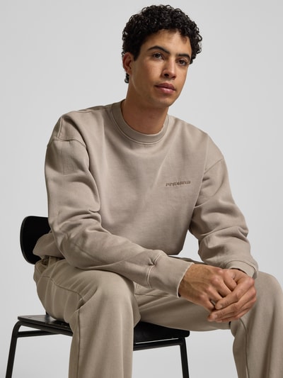 Männermodel trägt Oversized Sweatshirt mit Label-Stitching von Pegador, beige, Baumwoll-Mix, Rundhalsausschnitt, Nahaufnahme Oberkörper.