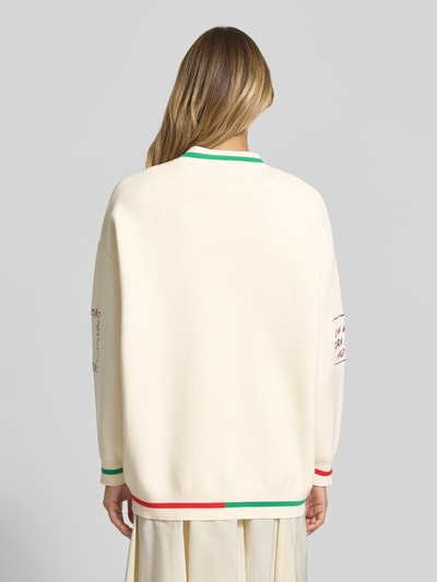 Frauenmodel trägt Loose Fit Strickjacke mit Viskose-Anteil Modell 'JASEBALL SNOOPY EMBO' von Essentiel Antwerp in Optik: Unifarben mit Kontraststreifen, Feinstrick, überschnittene Schultern, geripptem Rumpfabschluss und Langarm, Ganzkörperansicht Rückansicht.