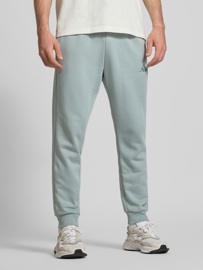 Männermodel trägt Sweatanzug mit Label-Stitchings von adidas Sportswear im Baumwoll-Mix, Regular-Fit, Nahaufnahme Unterkörper.