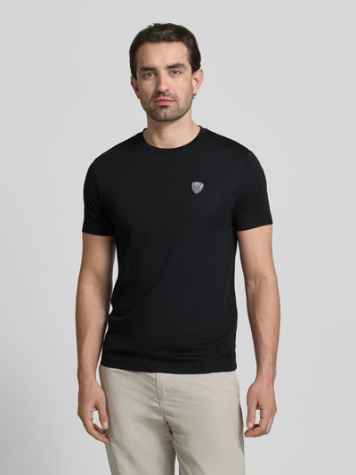 Męski model nosi T-Shirt aus Viskose-Mix mit Label-Patch od EA7 Emporio Armani, czarny, krój slim fit, z krótkim rękawem, widok całej sylwetki z przodu.