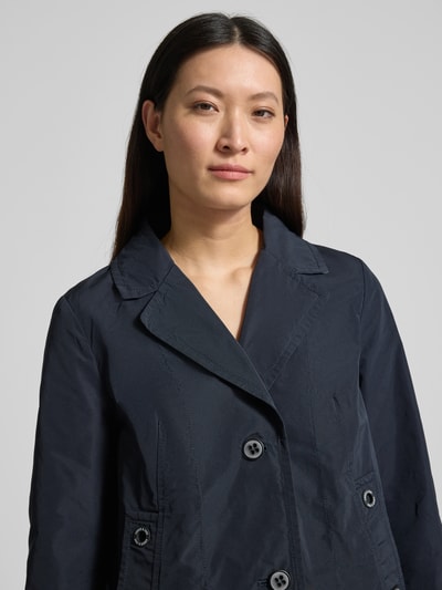 Modelka kobieca ma na sobie Kurtkę 'Jacke im 2-in-1-Look' od Amber & June, granatowy kolor, efekt 2 w 1, krój regular fit, kołnierz z połami, listwa guzikowa, detal z logo, długość tyłu w rozmiarze 36: 65 cm, szerokość ramion w rozmiarze 36: 42 cm, szerokość w rozmiarze 36: 51 cm, długość rękawów w rozmiarze 36: 63 cm, zbliżenie na górę ciała.