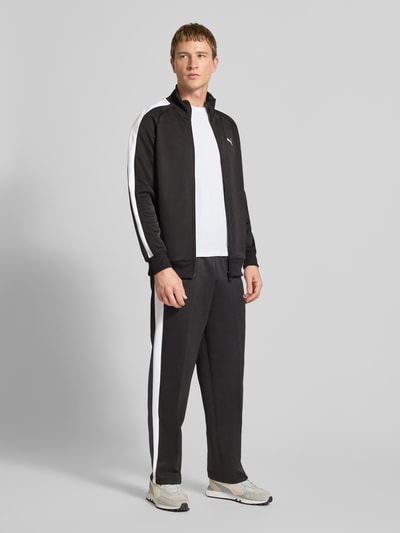Männermodel trägt Sweatjacke mit Label-Print von PUMA PERFORMANCE, Material-Mix mit Baumwoll-Anteil, Regular-Fit, Schwarz mit weißen Details, Reißverschluss, Stehkragen, Reißverschlusstaschen, gerippte Abschlüsse, Rückenlänge 73 cm, Ärmellänge 52 cm, Ganzkörperansicht von vorne.