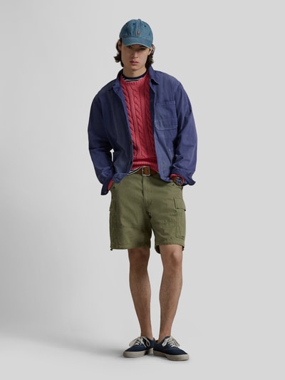 Męski model nosi Regular Fit Strickpullover aus reiner Baumwolle od Polo Ralph Lauren, różowy kolor, warkoczowy wzór, dzianina, bawełna, logo, długi rękaw, ściągacze, widok całej sylwetki z przodu.