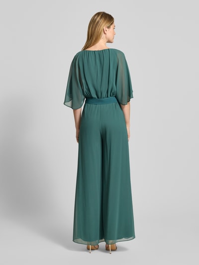 Frauenmodel trägt Jumpsuit aus fließendem Stoff mit Bindegürtel von Vera Mont in Grün, Chiffon, weites Bein, Ganzkörperansicht Rückansicht. Rückenlänge bei Größe 36: 146 cm, Brustweite 33 cm, Ärmellänge 30 cm, Gesamtlänge 147 cm, Innenbeinlänge 81 cm.