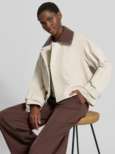 Männermodel trägt Jacke mit Ärmelriegeln Modell 'AVANTI' von YAS, krój regular fit, bawełniany miks, kołnierz wykładany, dwurzędowa, kieszenie wpuszczane, długość pleców w rozmiarze 36: 57 cm, szerokość ramion w rozmiarze 36: 54 cm, szerokość klatki piersiowej w rozmiarze 36: 58 cm, długość rękawa w rozmiarze 36: 57 cm, beżowe i brązowe kolory, gładka faktura. Ganzkörperansicht von vorne.