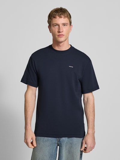Męski model nosi Regular Fit T-Shirt mit Logo-Print Modell 'True' von G-Star Raw, granatowy kolor, okrągły dekolt, krój regular fit, nadruk z logo, długość tyłu w rozmiarze M: 66 cm, Ganzkörperansicht von vorne.