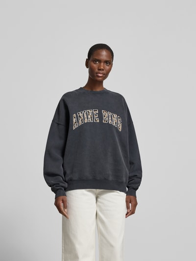 Frauenmodel trägt Oversized Sweatshirt aus Baumwolle von Anine Bing in dunklem Ton, Rundhalsausschnitt, elastische Abschlüsse, überschnittene Schultern, Rückenlänge bei Größe S 63 cm, Ganzkörperansicht von vorne.