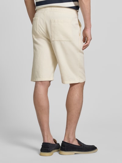 Męski model nosi Shorts aus Baumwolle mit elastischem Bund od JAKE*S STUDIO MEN w kolorze kremowym, krój regular fit, bawełna, szeroka tylna kieszeń, elastyczny pas z tunelem, szerokość w rozmiarze M: 47 cm, długość wewnętrzna nogawki w rozmiarze M: 26 cm, całkowity widok od tyłu.