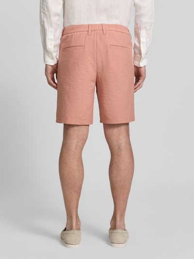 Mężczyzna nosi Regular Fit Bermudas aus Baumwoll-Mix Modell 'KARL' od SELECTED HOMME, jasnoróżowy, struktura seersucker, widok całej sylwetki z tyłu, kontekst: bermudy męskie, krój regular fit, paski, kieszenie, bawełniany miks.