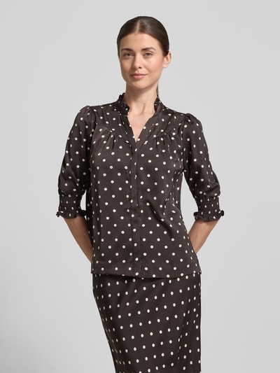 Kobiece modelka trägt Regular Fit Bluse mit Stehkragen Modell 'Diana' von Neo Noir z obszyciem falbanami, rękaw o dł. 1/2, elastyczne wykończenia, długość tyłu w rozmiarze 36: 59 cm, długość rękawów w rozmiarze 36: 41 cm, czarny kolor z białymi grochami, gładka faktura, ganzkörperansicht von vorne.
