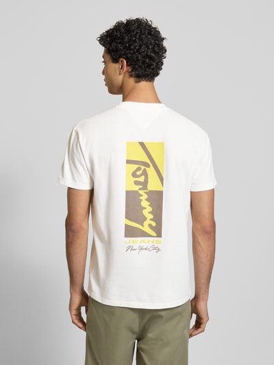 Männermodel trägt Regular Fit T-Shirt aus reiner Baumwolle Modell 'SIGN BLOCK' von Tommy Jeans, Optik: Unifarben, Rücken-Print in Gelb und Braun, kurzarm, Rundhals, Ganzkörperansicht Rückansicht.