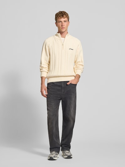 Männermodel trägt Regular Fit Strickpullover aus reiner Baumwolle mit Zopfmuster von PROHIBITED, cremefarben, Zopfmuster, Troyer-Kragen, Logo-Stickerei, Raglanärmel, gerippte Abschlüsse, Strick-Optik, Ganzkörperansicht von vorne.