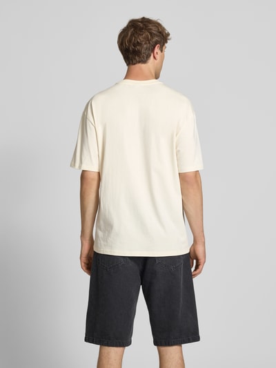 Männermodel trägt Oversized T-Shirt mit Logo-Stitching von KARL KANI, czysta bawełna, krój oversized fit, kremowy, widok całej sylwetki z tyłu.