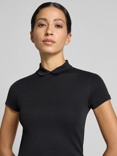 Frauenmodel trägt Slim Fit T-Shirt mit hochschließendem Polokragen von Marc Cain aus Baumwoll-Elasthan-Mix in Schwarz, Nahaufnahme Oberkörper.