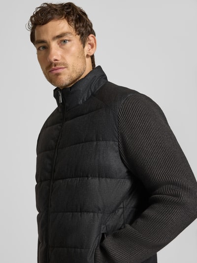 Männermodel trägt Steppjacke mit Stehkragen und Zweiwege-Reißverschluss von Christian Berg Men in Schwarz, Nahaufnahme Oberkörper, Regular Fit, feine Rippenstruktur an den Ärmeln, strukturierte Oberfläche, Reißverschlusstaschen, KI-modifiziertes Bild.