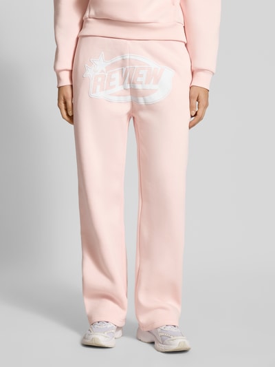 Frauenmodel trägt Straight Leg Sweatpants mit Logo und elastischem Bund von Review, hellrosa, Baumwoll-Mix, Ganzkörperansicht von vorne.
