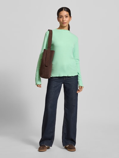 Modelka kobieca ma na sobie Slim Fit Langarmshirt mit Viskose-Anteil od s.Oliver RED LABEL, jednolity kolor, struktura prążkowanego dzianinowego materiału, wysoki dekolt, długie rękawy i wykończenia frill, z naszywką z logo; krój slim fit; widok całej sylwetki z przodu.