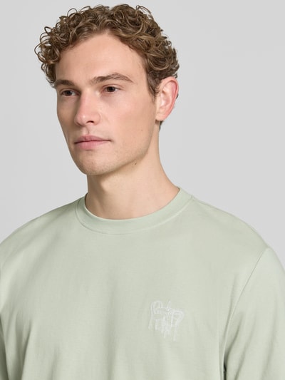 Męski model nosi Regular Fit T-Shirt aus reiner Baumwolle Modell 'HASPEN' von SELECTED HOMME, jednokolorowy, dżersej, wyhaftowany motyw, okrągły dekolt, krótki rękaw, materiał: czysta bawełna, zbliżenie na górną część ciała.