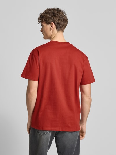 Männermodel trägt rotes T-Shirt mit Label-Stitching und Rundhalsausschnitt von Carhartt Work In Progress, Baumwolle, Rückansicht, Ganzkörperansicht.