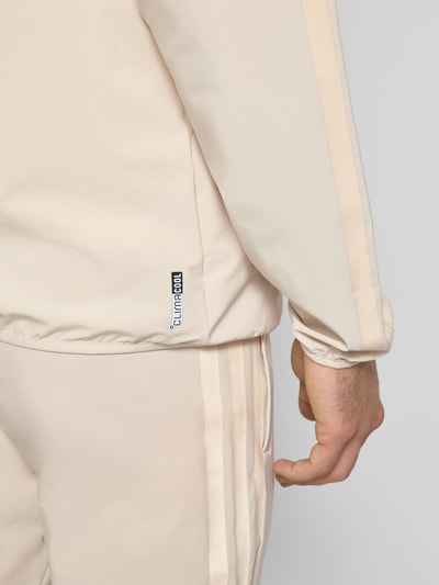 Männermodel trägt trainingsjack met capuchon van adidas Sportswear in materiaalmix met stretch en labelprint, detailaufnahme rechterarm.